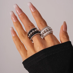 Detailed view of layered beaded rings with white pearls and black beads on fingers