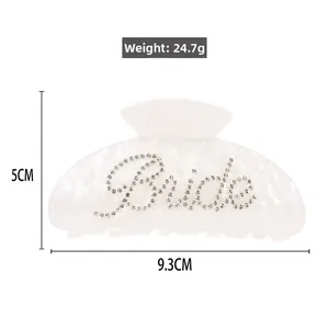 Macro detail of white marble acrylic hair claw with Bride rhinestone lettering