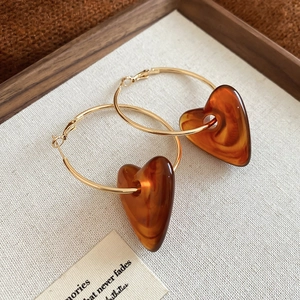 Detailed view of golden hoop earrings with amber resin heart pendants on white fabric
