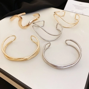 Detail view of minimalist gold and silver minimalist wavy cross open cuff bracelets