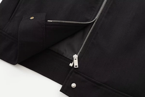 Detail of black twill jacket featuring silver metal zipper and snap button closure