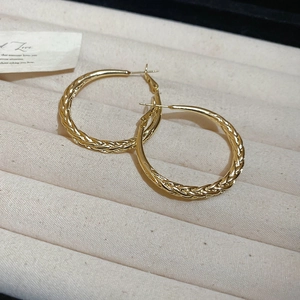 Detail of gold twisted hoop earrings with textured metal weave on a velvet tray