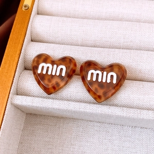 Detail of tortoise shell heart stud earring with white logo on beige velvet display