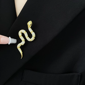 Detail of a gold snake brooch with white crystals pinned on a black suit lapel