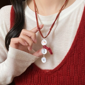 Detail of snowman pendant with red tassel and suede cord on a white knit sweater