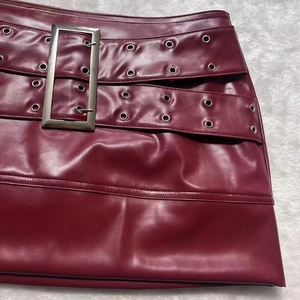 Detailed macro view of burgundy PU leather skirt with silver buckle and eyelet belt