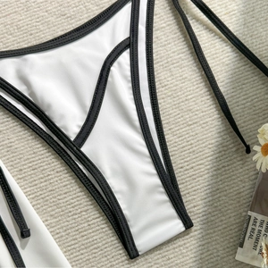 Close-up of minimalist white bikini bottoms with black trim on woven resort background