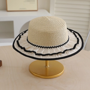 Detail of summer straw hat with lace ruffled brim and black ribbon trim on gold stand