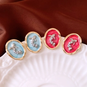 Close-up of oval enamel earrings with koi fish and pearl details on a ceramic dish