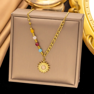 Dettaglio della collana con ciondolo a sole dorato e perle colorate su sfondo di seta