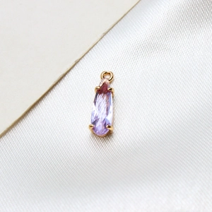 Macro shot of purple teardrop crystal pendant in gold setting on white silk