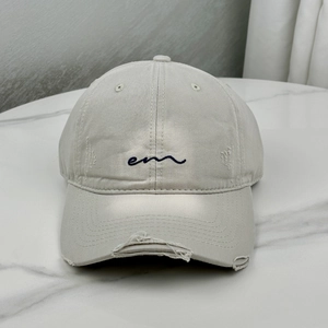 Close-up of beige distressed cotton baseball cap with blue embroidered logo and frayed brim
