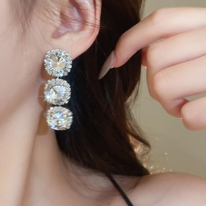 Close-up of silver drop earrings featuring triple square-cut crystals and halo diamonds