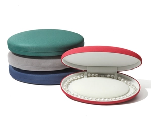 Detailed view of oval velvet jewelry boxes in green, grey, blue and red with pearl necklace