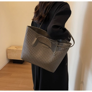 Detailed shot of large grey woven leather tote bag held by a model in a minimalist room