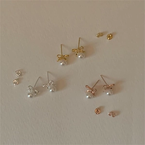 Bow pearl stud earrings shown in gold, silver, and rose gold finishes on textured paper