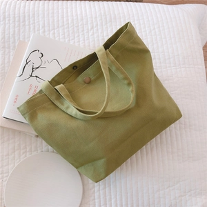 Detail shot of grass green canvas tote bag featuring brass snap button and thick handles