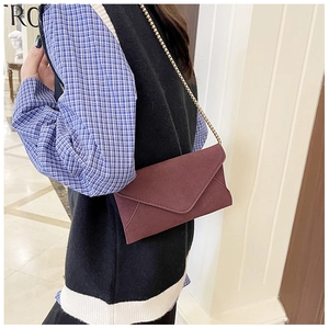 Detail of burgundy frosted suede envelope bag featuring a minimalist gold chain strap