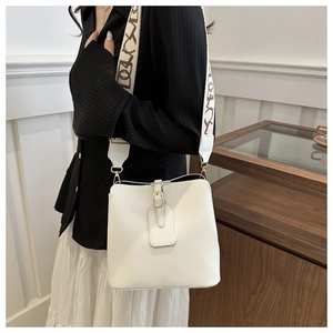 Detail of white lychee leather bucket bag featuring a wide patterned strap and gold hardware