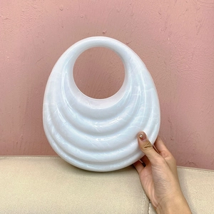 Detail showing white acrylic handbag with ripple wave texture and circular handle grip