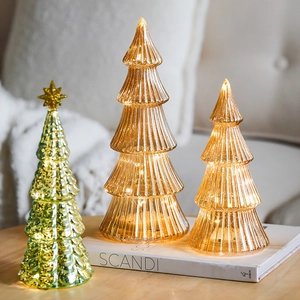 Three glowing glass Christmas trees with LED lights in amber and green on a white book