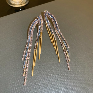 Detail of gold tassel earrings featuring blue and pink rhinestones on a textured surface
