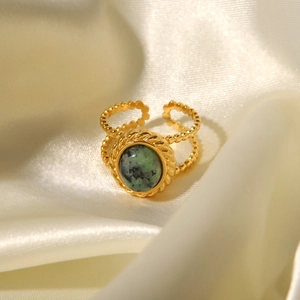 Close-up of vintage gold twist ring featuring an inlaid green natural stone on silk fabric