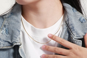 Close-up of a minimalist gold snake bone chain necklace worn with a denim jacket