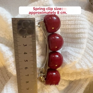 Detailed view of an 8cm cherry-shaped spring hair clip with red glossy beads and metal base