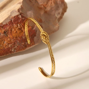 Minimalistischer goldener Edelstahl-Knotenarmreif präsentiert auf einem roten Naturstein