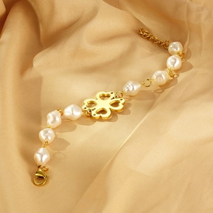 Detailed macro of gold clover bracelet with baroque pearls on silk champagne fabric