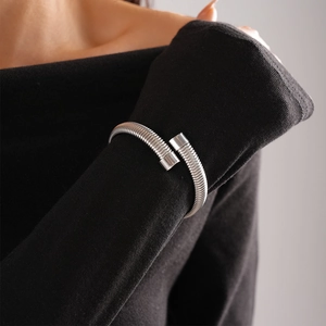 Detail of silver stainless steel snake spiral cuff bracelet worn over black sleeve
