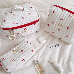 Detailed set of three quilted cosmetic bags with red cherry prints and handle straps