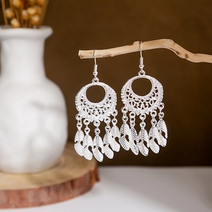 Detail view of ethnic silver earrings with hollow circular patterns and feather tassels