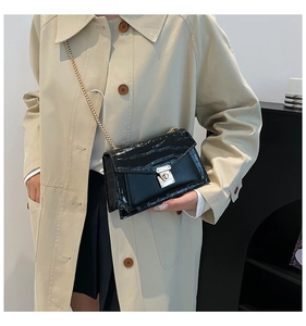 Detail of black crocodile texture chain bag worn with a beige trench coat