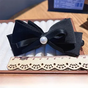 Detail shot of a 9cm black satin bow hair clip with pearl on white velvet tray