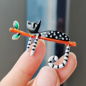 Détail d'une broche en émail représentant un chat noir et blanc sur une branche d'orange