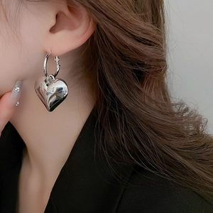 Close-up of polished silver heart drop earrings worn on a model with long brown hair