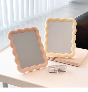 Pink and beige cream-colored wavy frame makeup mirrors on a sunlit tabletop