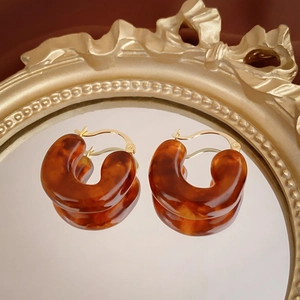Detail of C-shaped amber resin earrings with retro texture on a gold embossed mirror