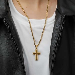 Close-up of a gold cross pendant necklace on a model wearing a black leather jacket