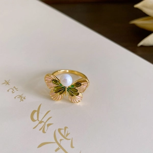 Detail of vintage gold butterfly ring with pink and green enamel and pearl on a notebook