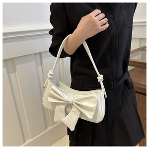 Detail of white glossy leather underarm bag featuring a large bow and knotted shoulder strap