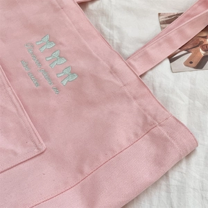 Détail du sac en toile rose montrant la broderie de nœud bleu et le slogan brodé