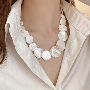 Detail of layered white seashell pendant necklace on woman wearing a white shirt