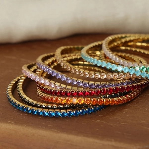 Stack of gold plated tennis bracelets with colorful zircon stones on wooden surface