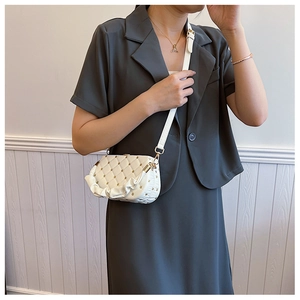 Close-up of white quilted crossbody bag featuring gold studs and ruffle strap detail