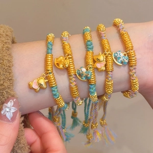 Macro detail of hand-woven colorful red rope bracelets with gold charms and enamel pendants