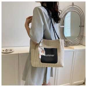 Détail d'un grand sac cabas en paille tissée avec bandoulière noire et foulard fleuri