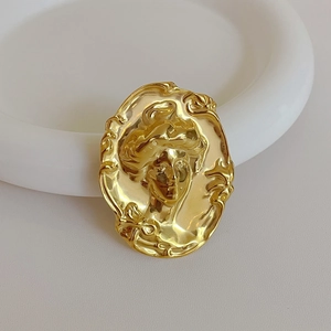 Vue détaillée d'une broche vintage dorée avec portrait de femme en relief sur fond blanc